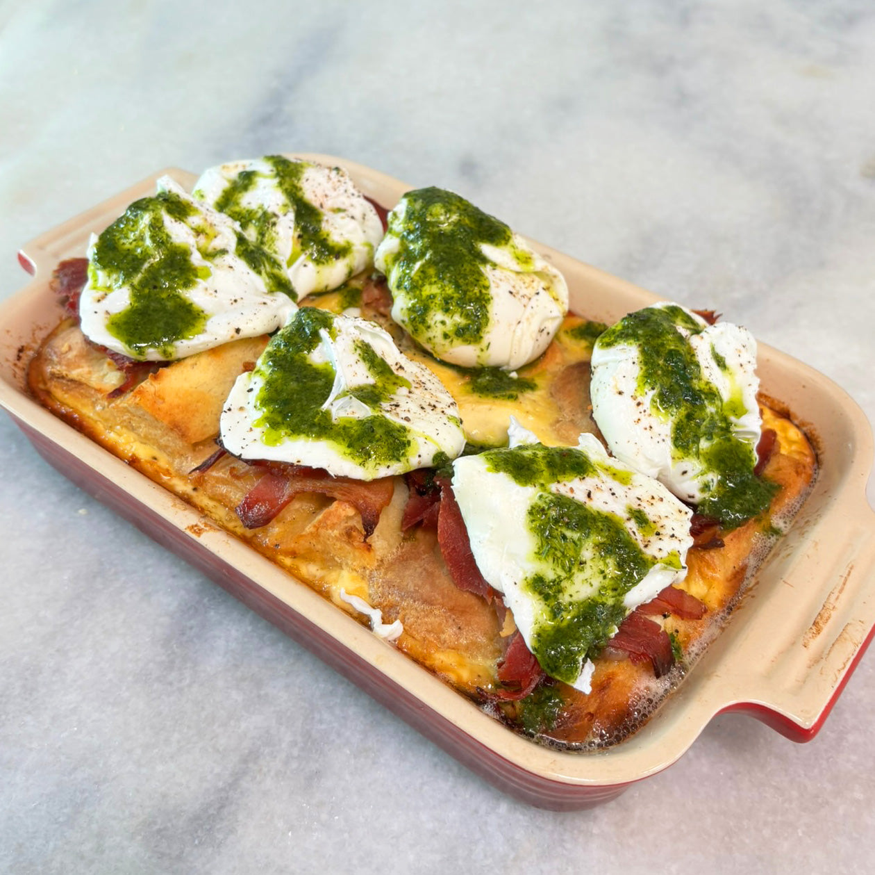 Biscuit "Benedict" Bake in red casserole dish topped with poached eggs and green herb pistou